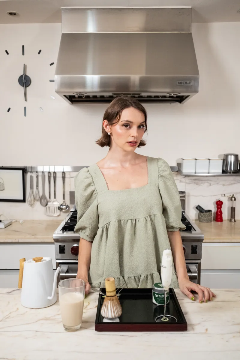 Woman at a kitchen counter with a bamboo whisk, kettle, and MyMatcha tin